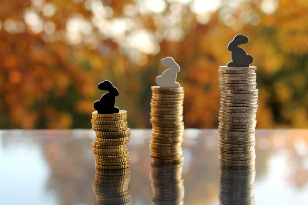 coins in a stack of EU cash with a model house and colored bunnies against a blurred background autumn landscape in backlight, housing concept, on credit, white and gray wages